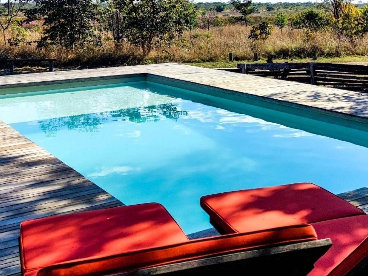 Two red sun loungers in the foreground and a medium-sized outdoor pool surrounded by a wooden deck with views of the Cerrado wilderness.