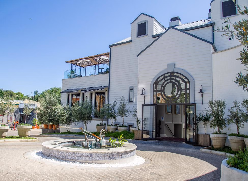 A white-painted timber building with black-framed windows and glass doors, opening to a courtyard with water features and plants.