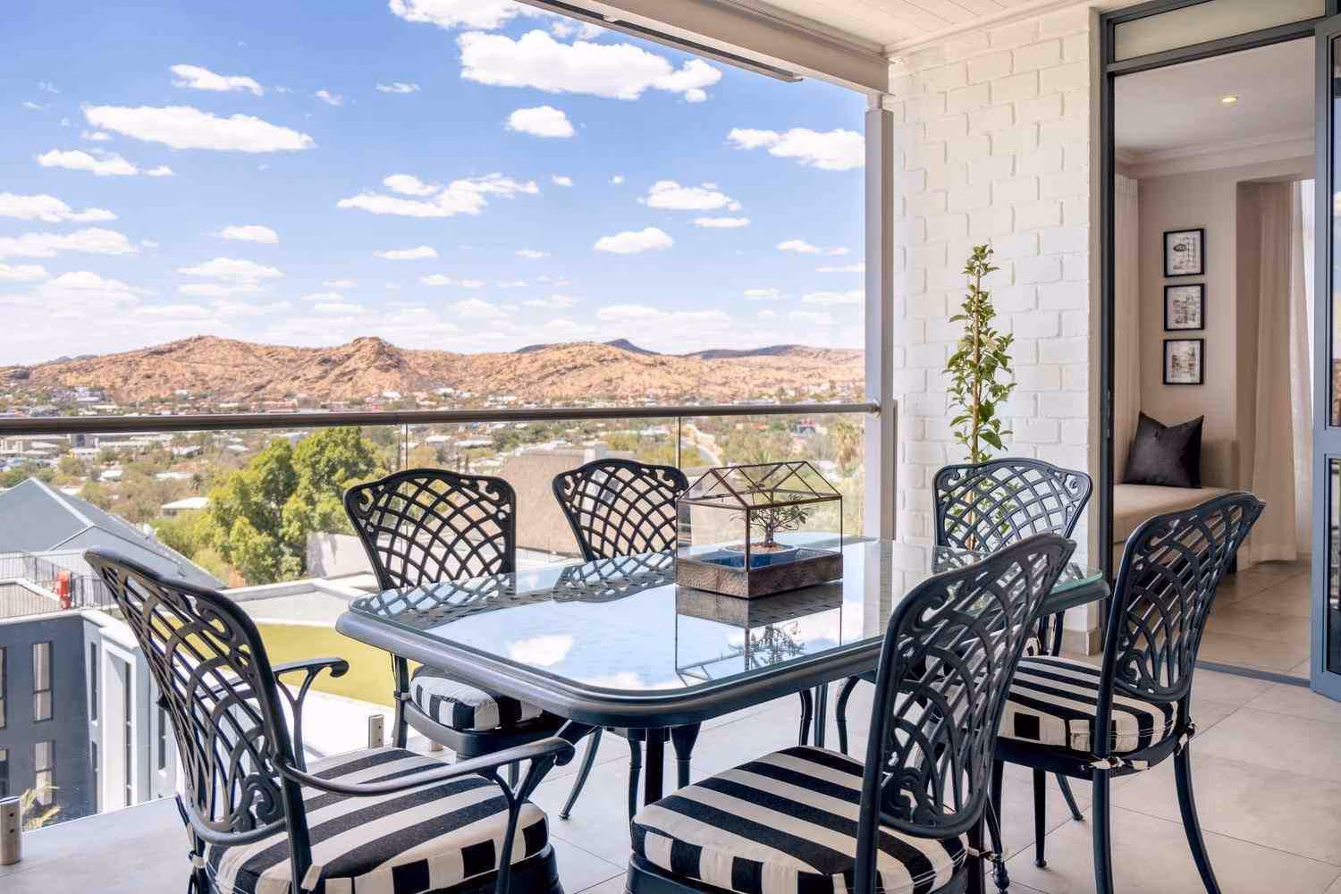 A glass-topped table with eight chairs and a bonsai tree decoration, placed on an open-sided terrace with views of the Auas Mountains