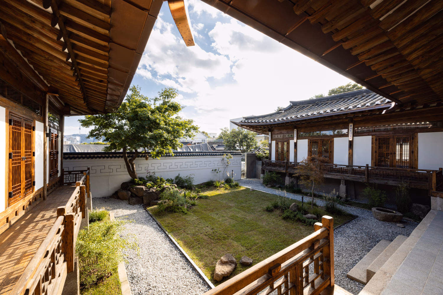 A traditional Korean hanok house in daytime with a tree growing in the centre and views of Seoul's skyline in the distance.