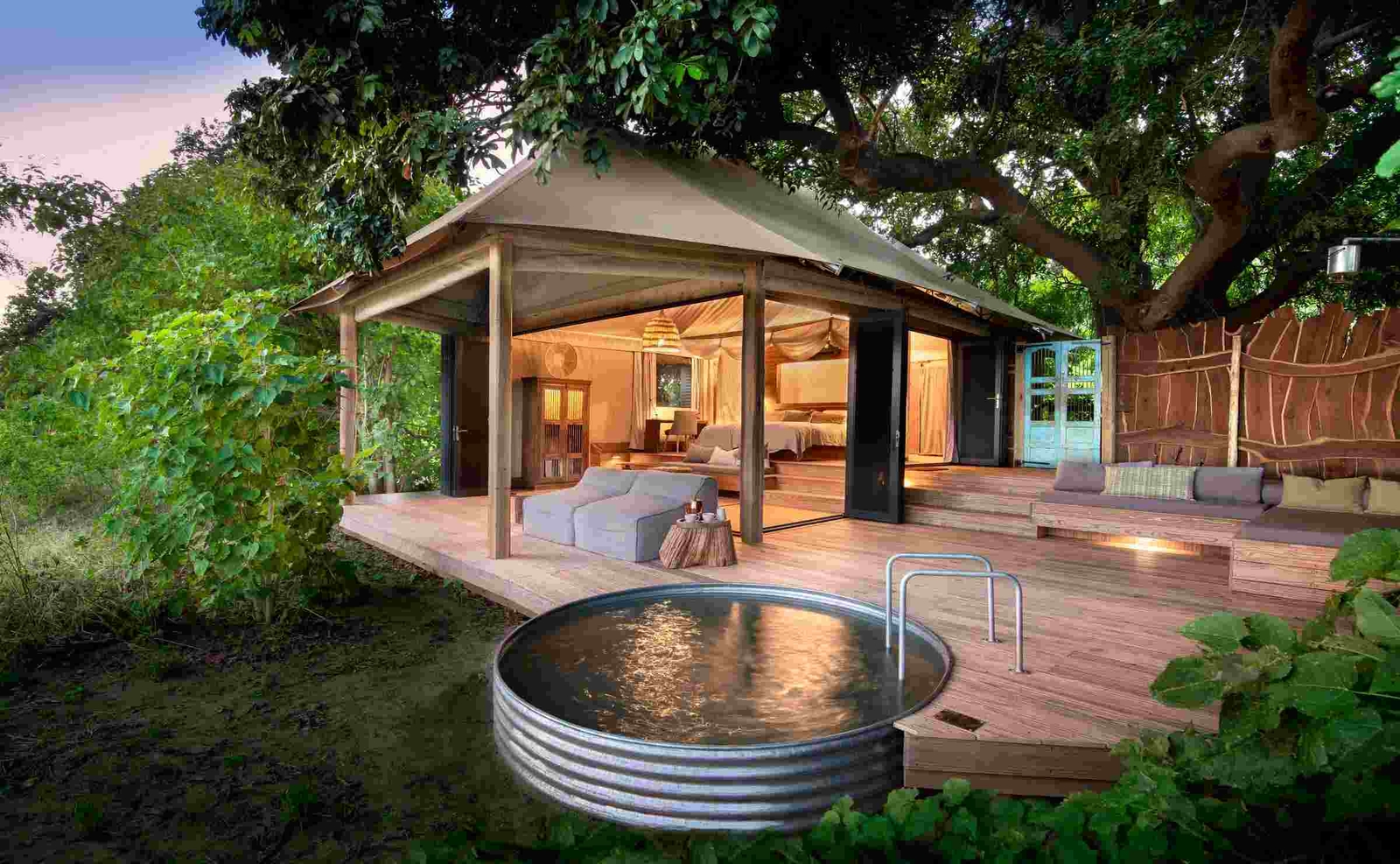 A view of a wooden deck with a plunge pool and a luxury suite behind. The sides of the tented room are open to the outside.