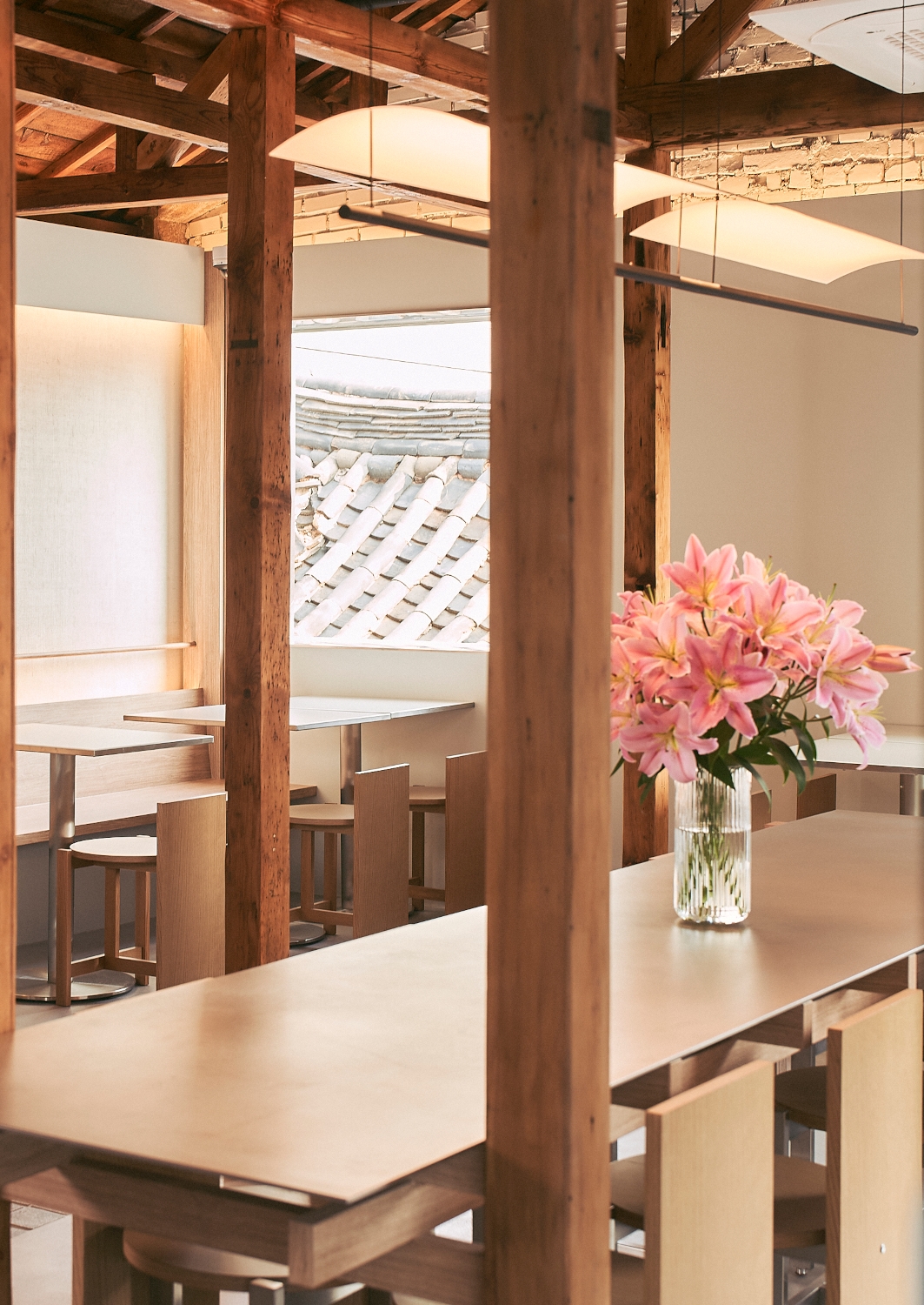 Interior of a cafe in a traditional Korean hanok house hotel with exposed beams, white walls and a pink floral arrangement in a vase on the counter.