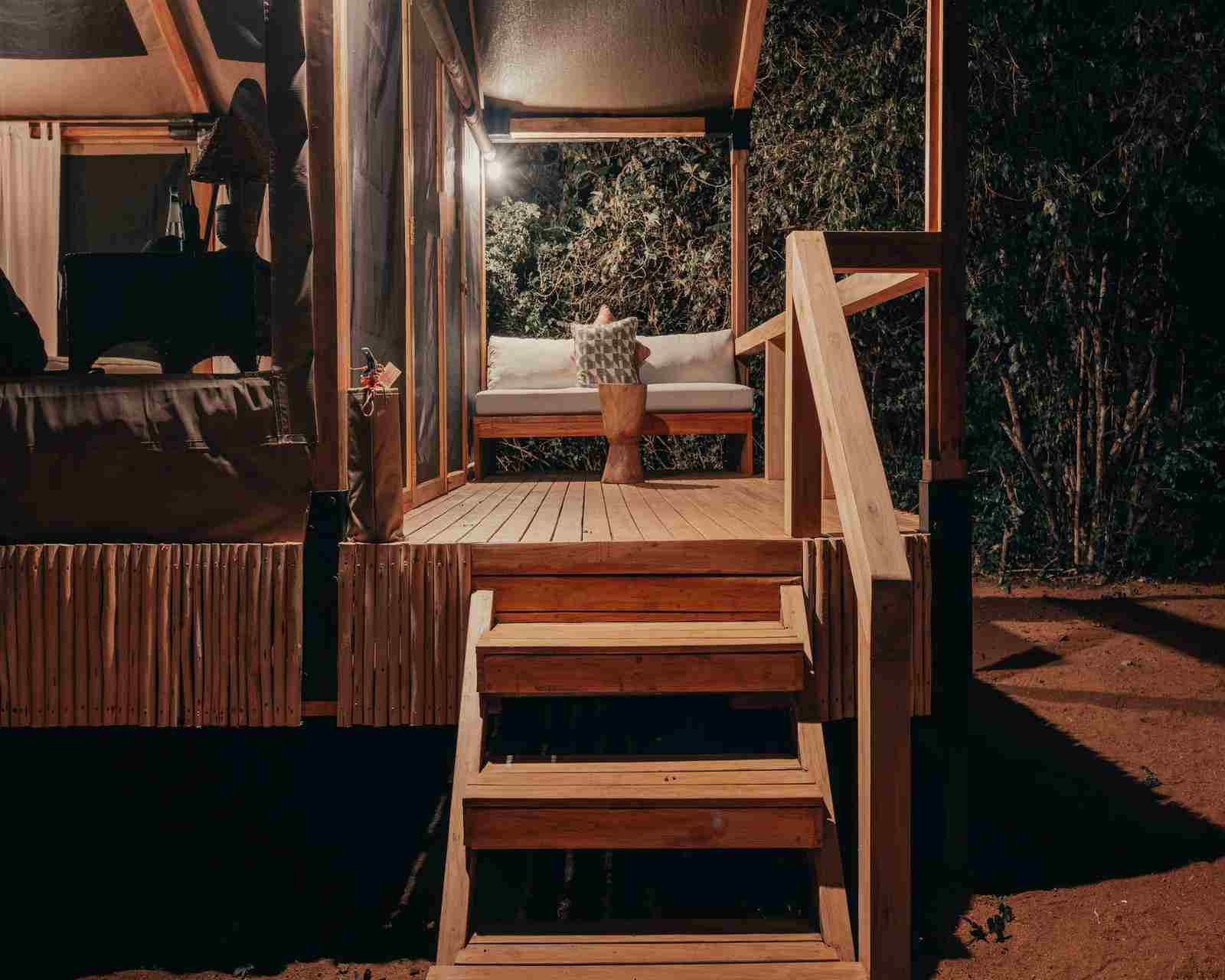 A nighttime scene showing three wooden steps leading to a deck with seating, with access to the tented suite on the left of the image.