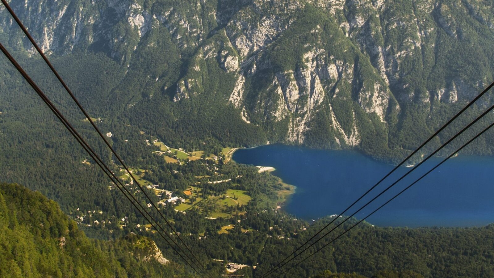 View down cable car support wires from the top of a mountains to a still blue lake