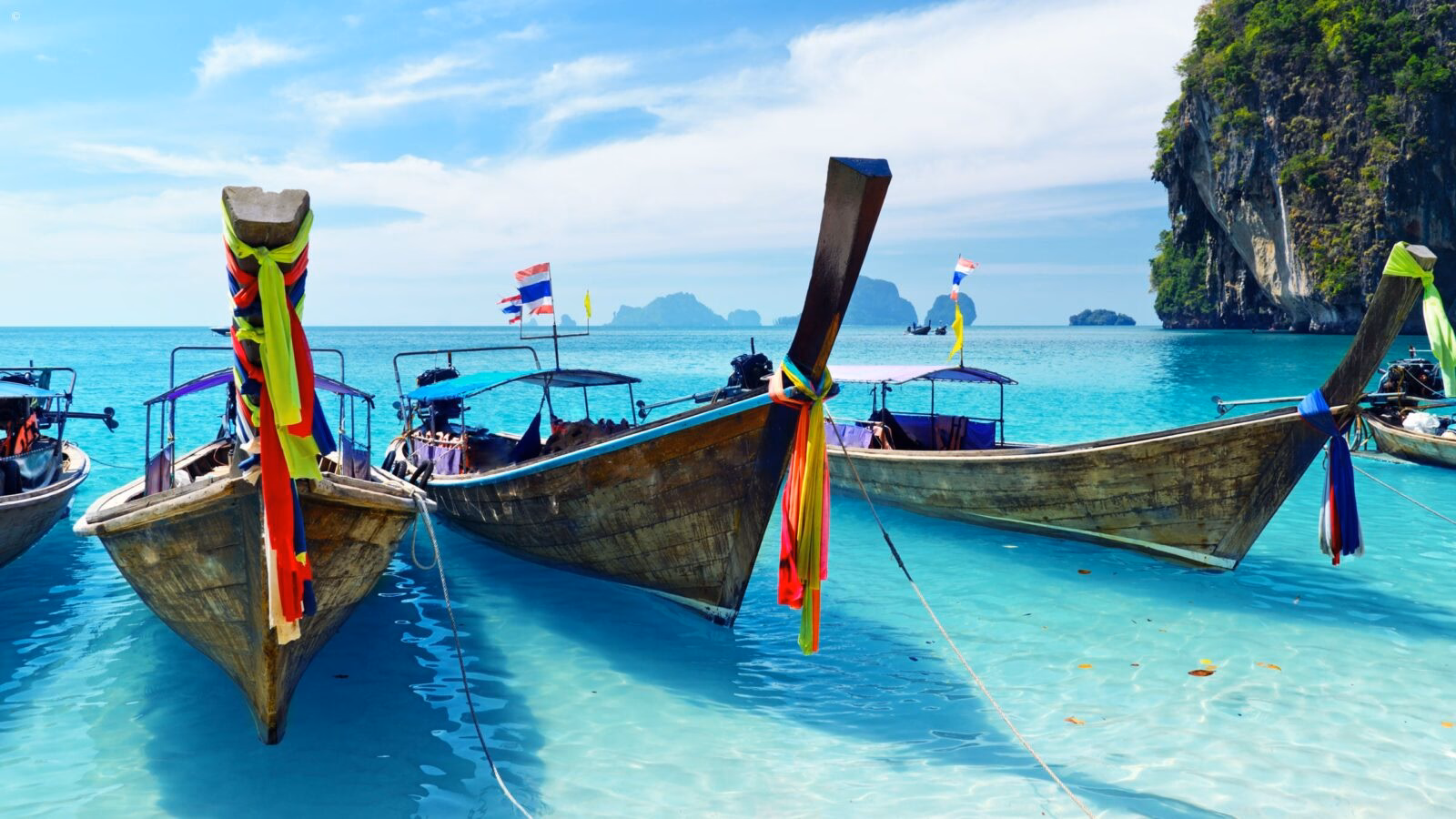 Traditional longtail boats with colorful ribbons rest in crystal clear shallow water for luxury Asia honeymoons.