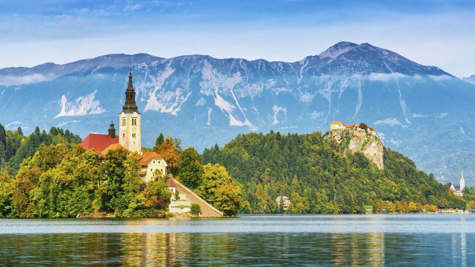 View of church on a small island in the middle of Lake Bled, an alpine lake in Slovenia with snow-capped mountains around it