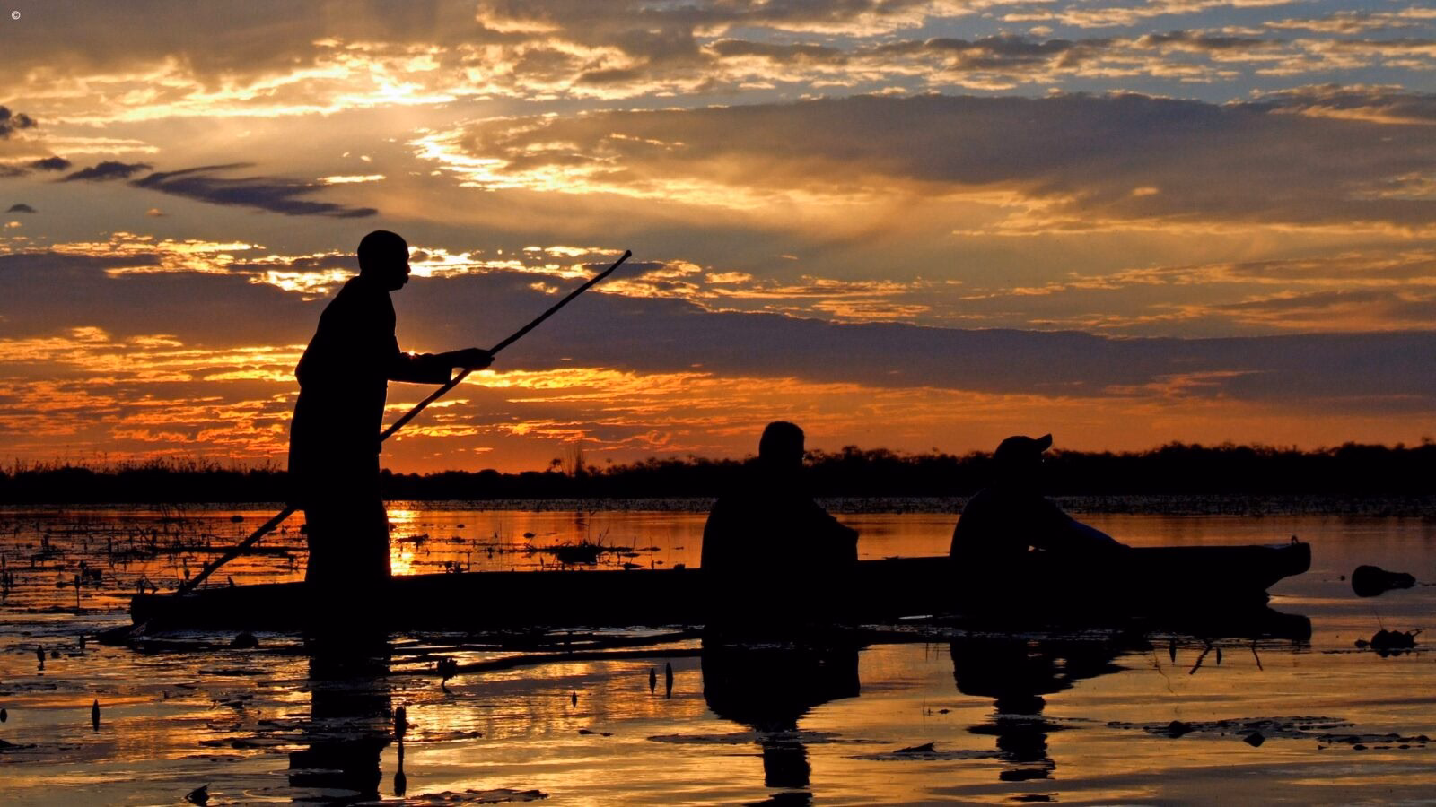 Silhouetted people in a boat at sunset on luxury Okavango Delta Tours.