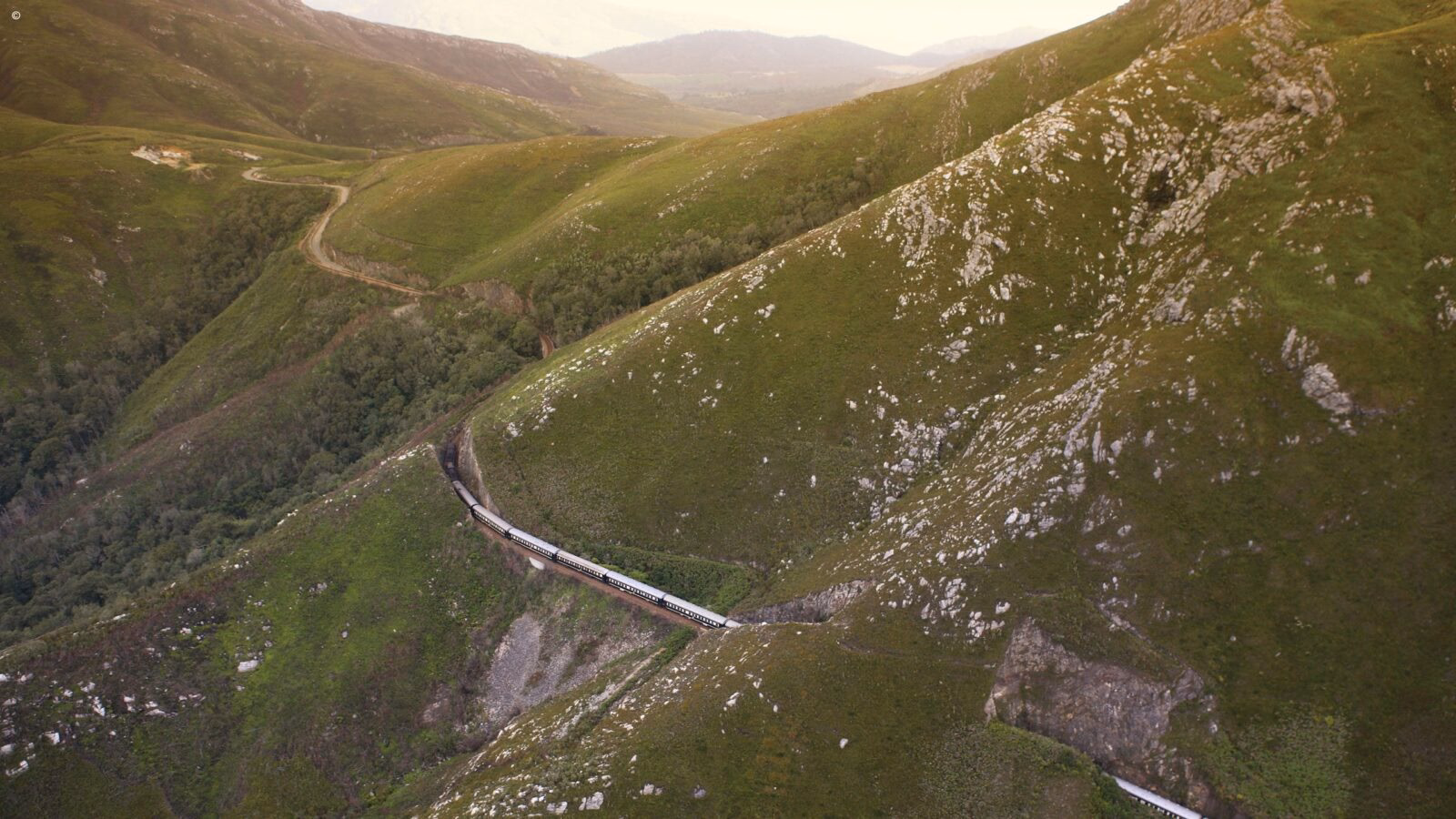 High-angle view of a luxury South Africa rail vacations train curving along a steep mountain ridge.
