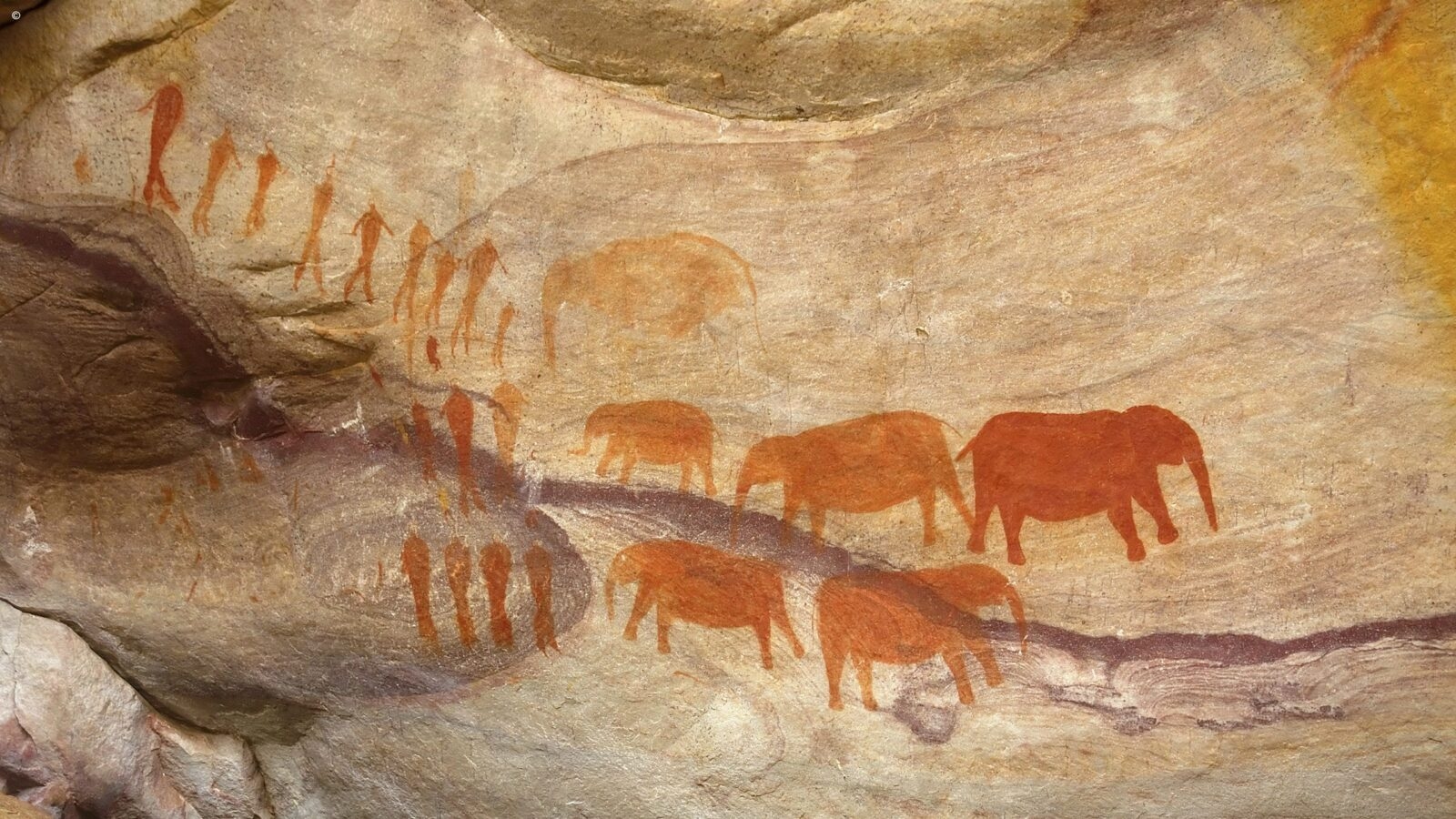 Ancient orange-hued rock art showing elephants and human figures, seen during luxury Western Cape trips.