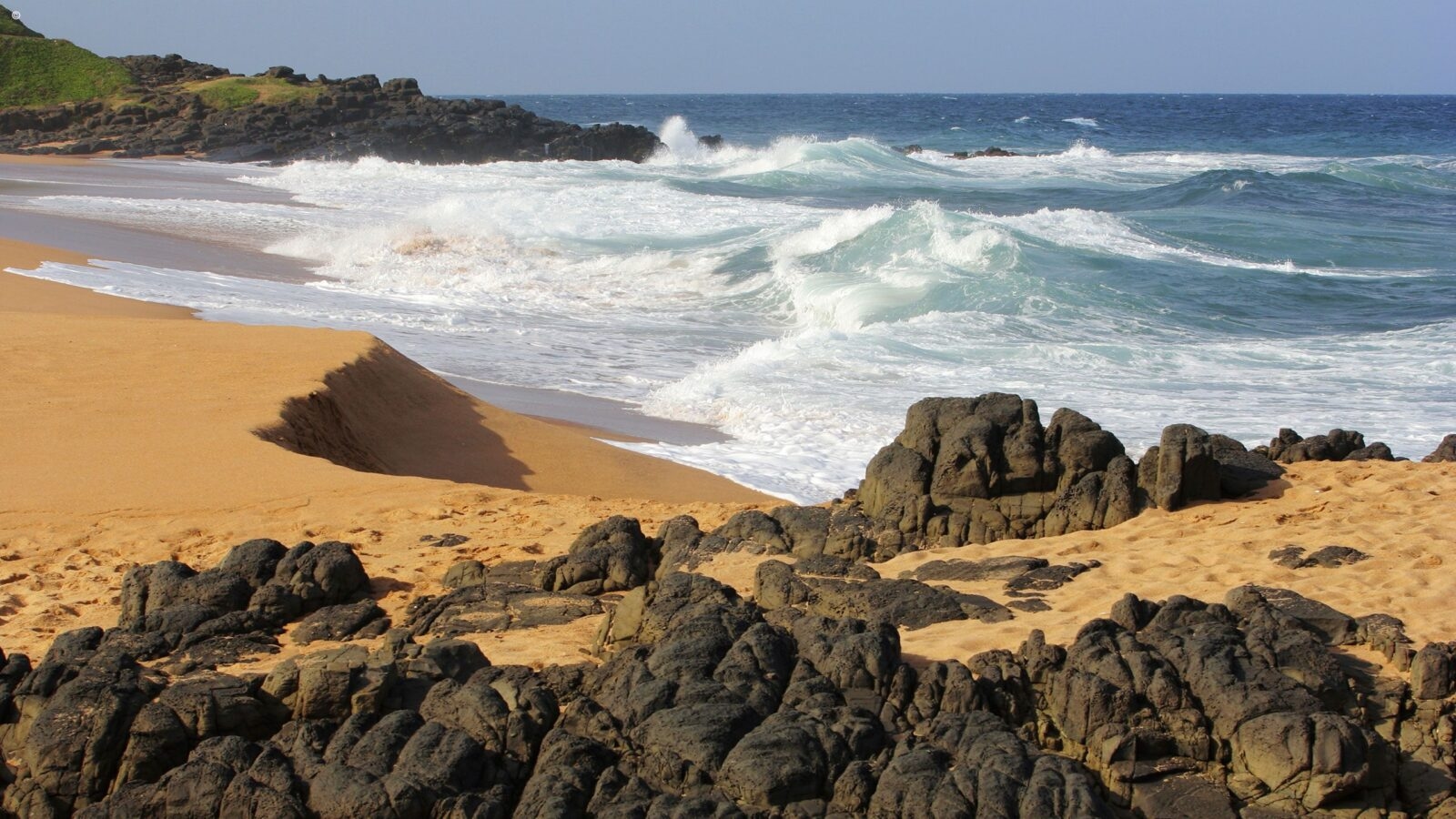Large ocean waves breaking on a sandy beach with dark rocks in the foreground during luxury Phinda safaris.