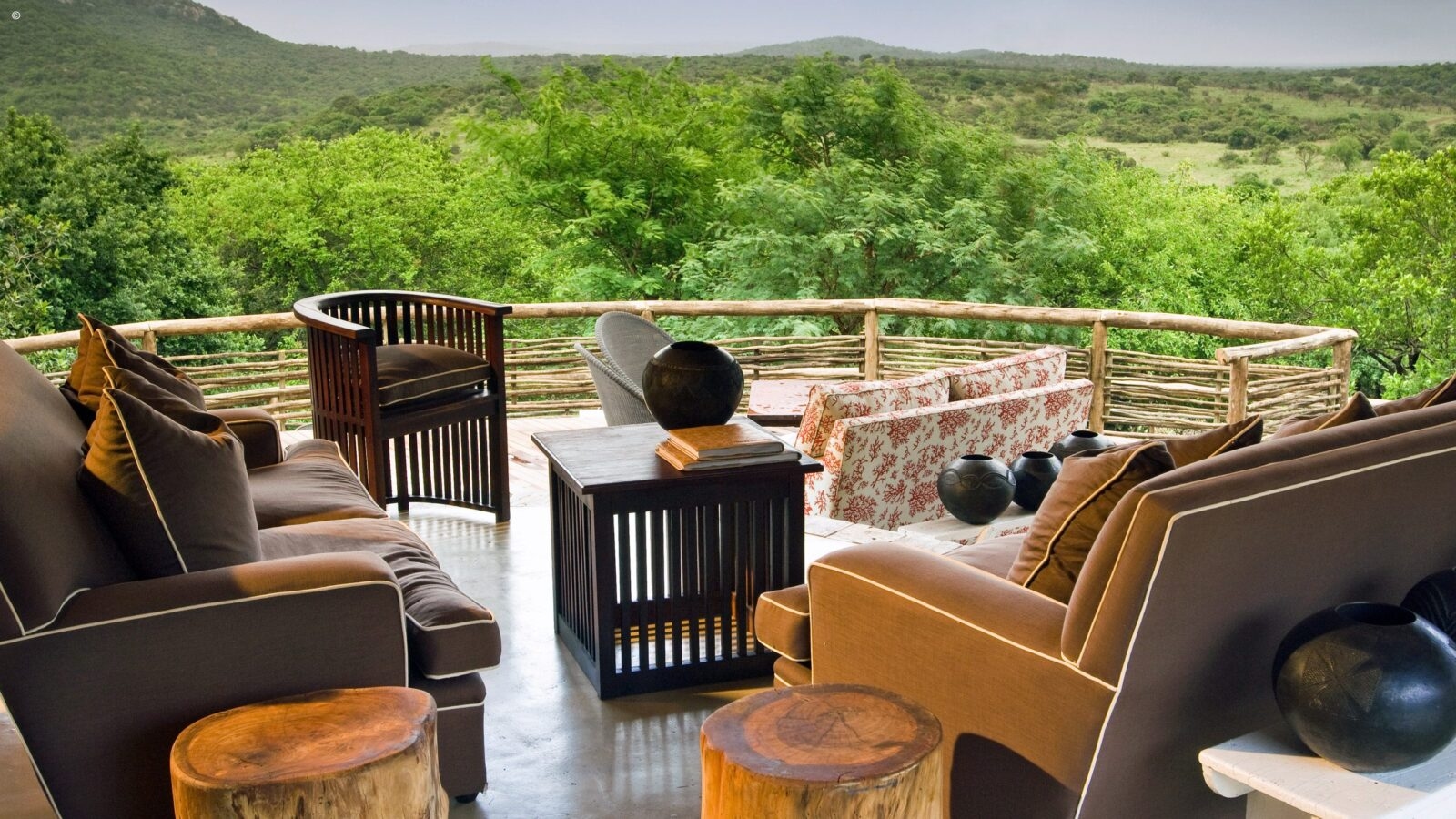 A luxury lodge deck with brown sofas and a view of green hills during luxury Phinda tours.