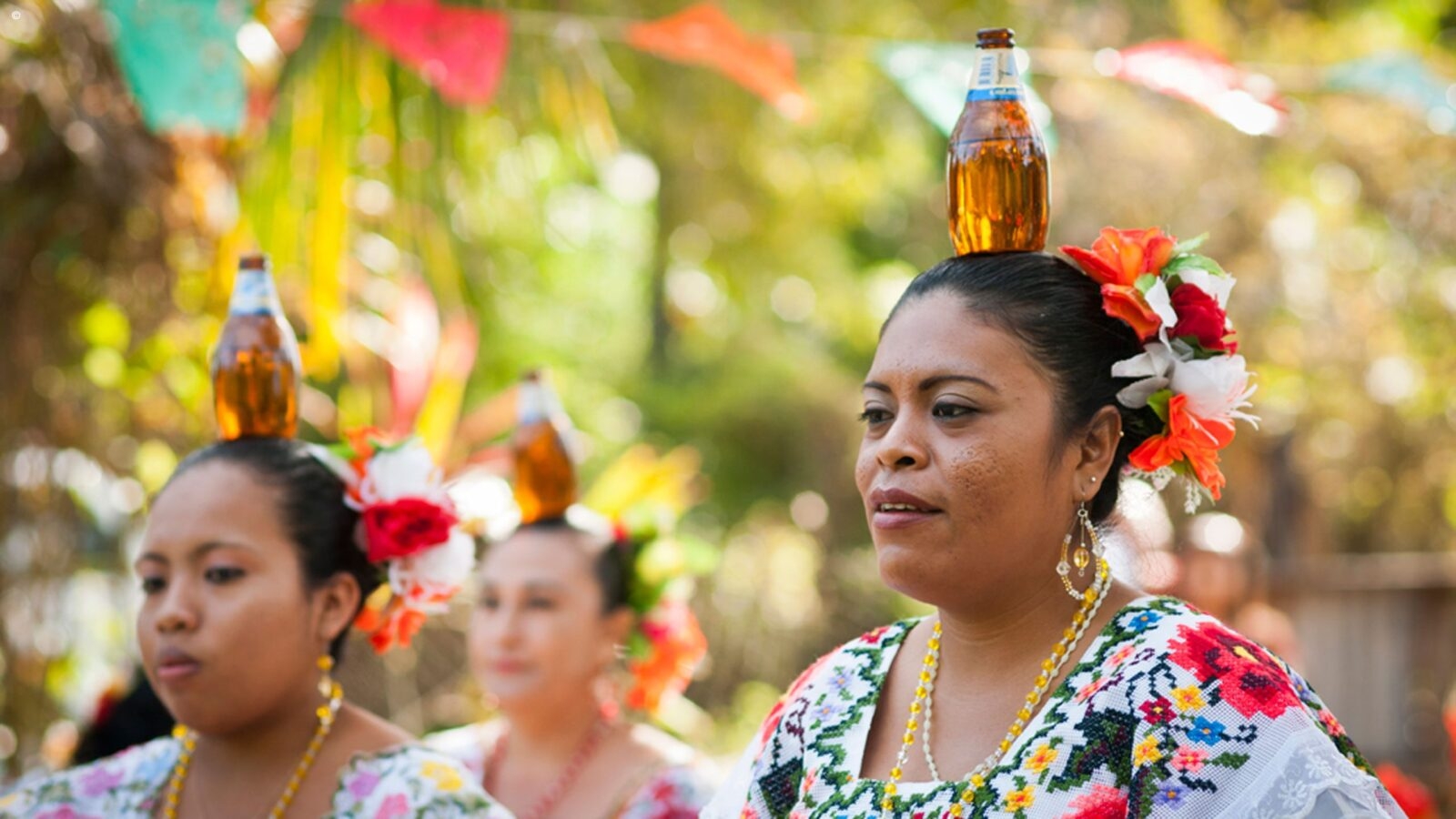 Women in traditional clothing balancing bottles on their heads during luxury Belize tours.