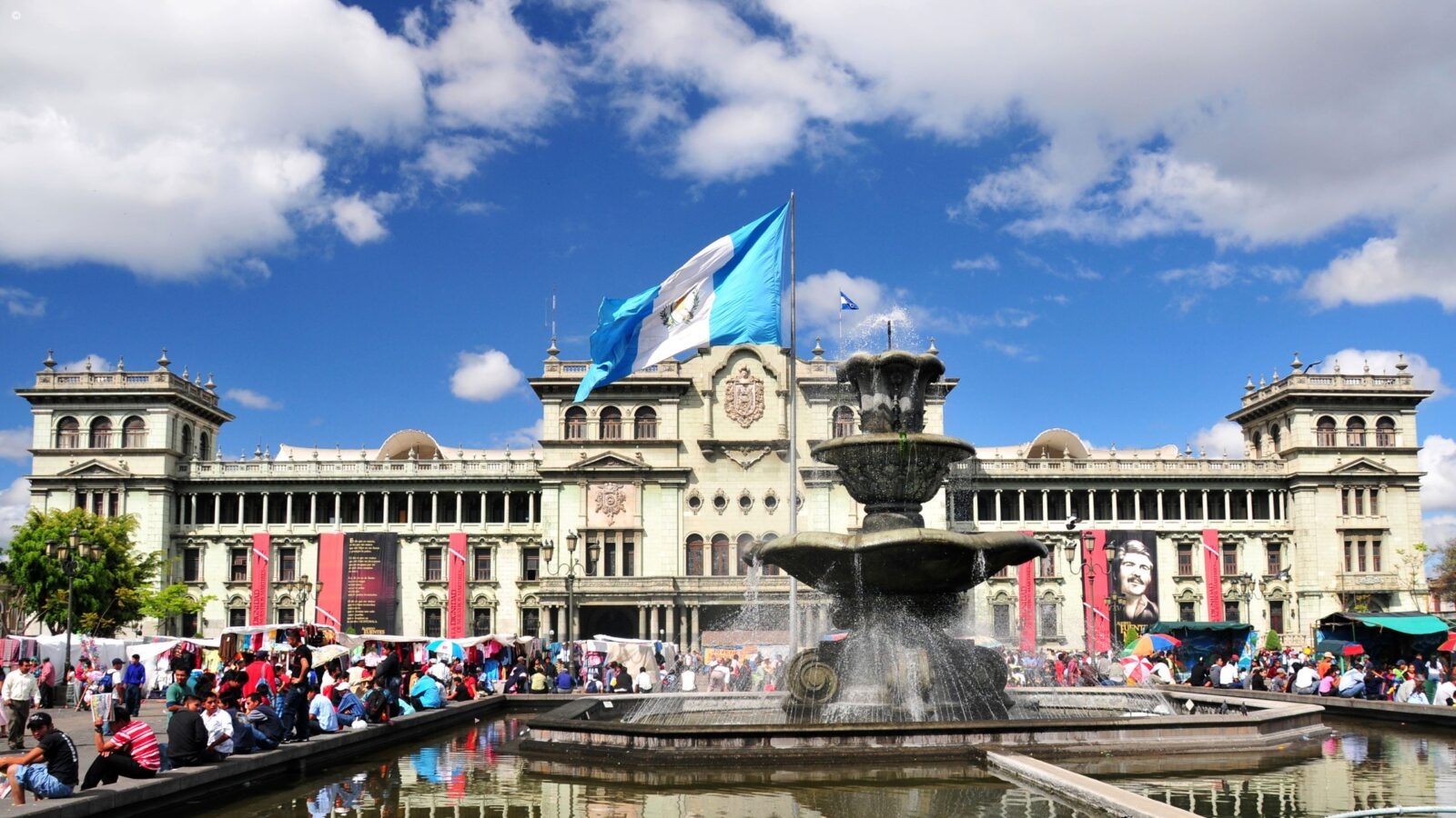 The fountain of Constitution Plaza lined with locals on a sunny day, Guatemala City in Guatemala