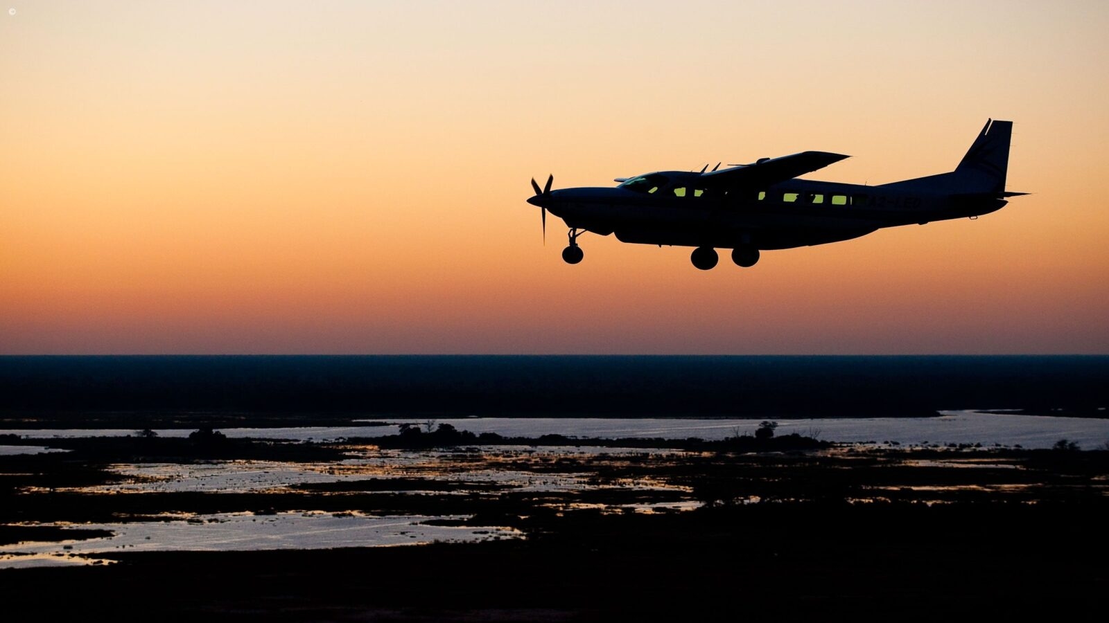 Silhouette of a bush plane flying over a delta at sunset on a Grand Tours of Africa journey.