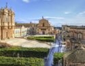 A wide view of a large baroque cathedral and public square with green hedges in Sicily.