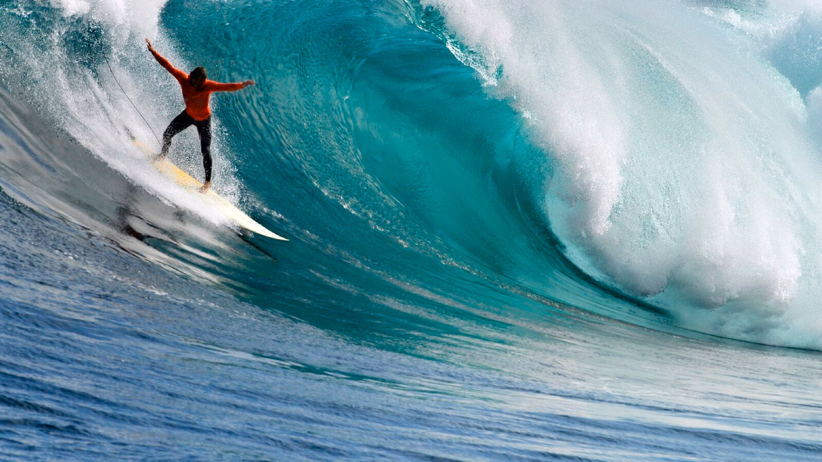 A surfer in an orange shirt riding a giant turquoise wave during luxury Eastern Cape vacations.