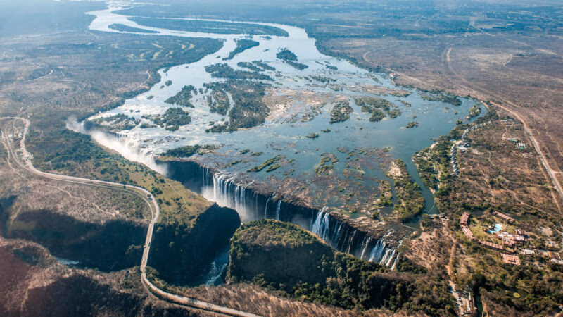 High-angle aerial view of the wide Zambezi River plunging over the edge of the large Victoria Falls waterfall.