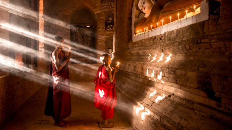 Young monks holding candles in a sunlit ancient temple during luxury asian family trips.