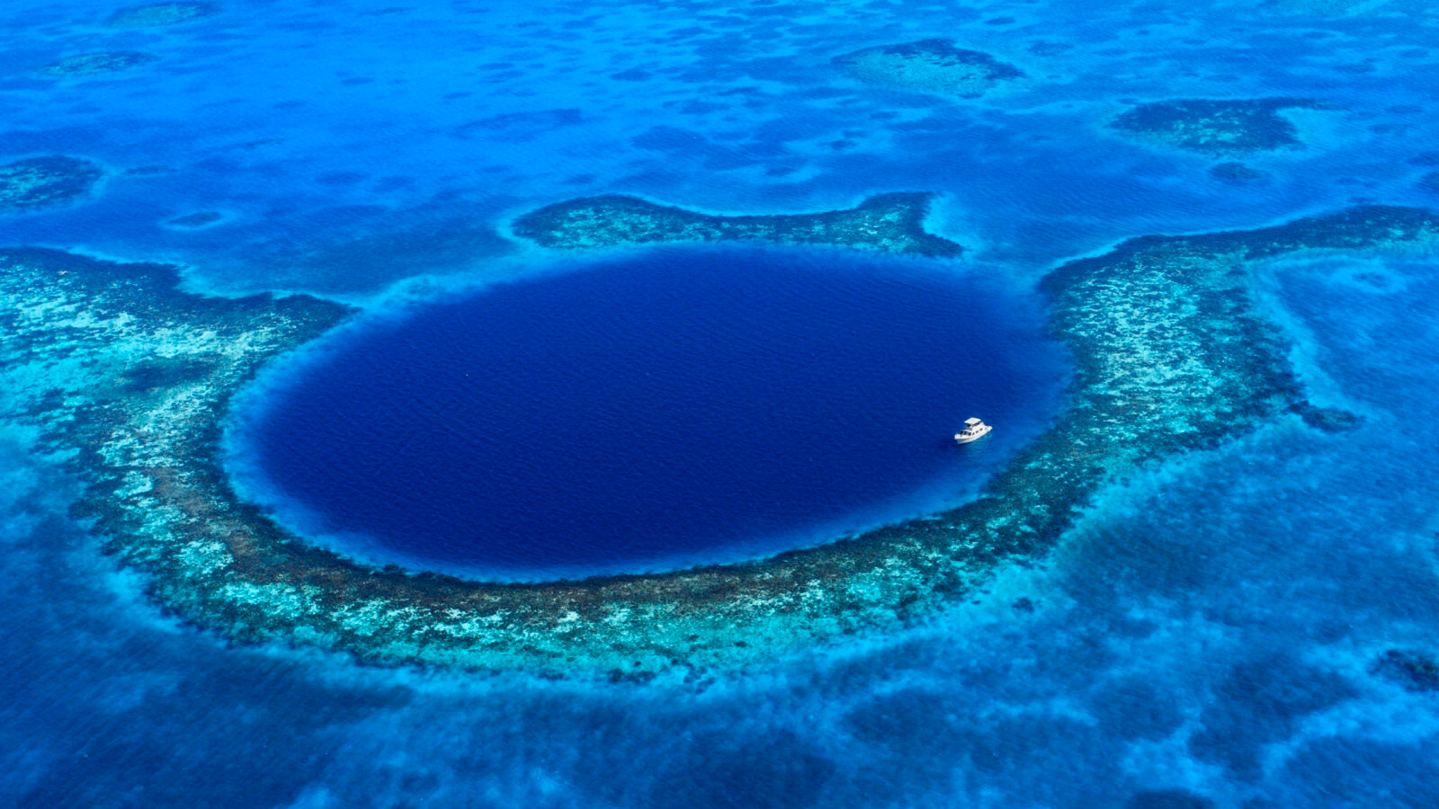 Aerial view of the Great Blue Hole, a large, deep blue, circular sinkhole surrounded by a shallow coral reef. Essential for luxury Belize tours.