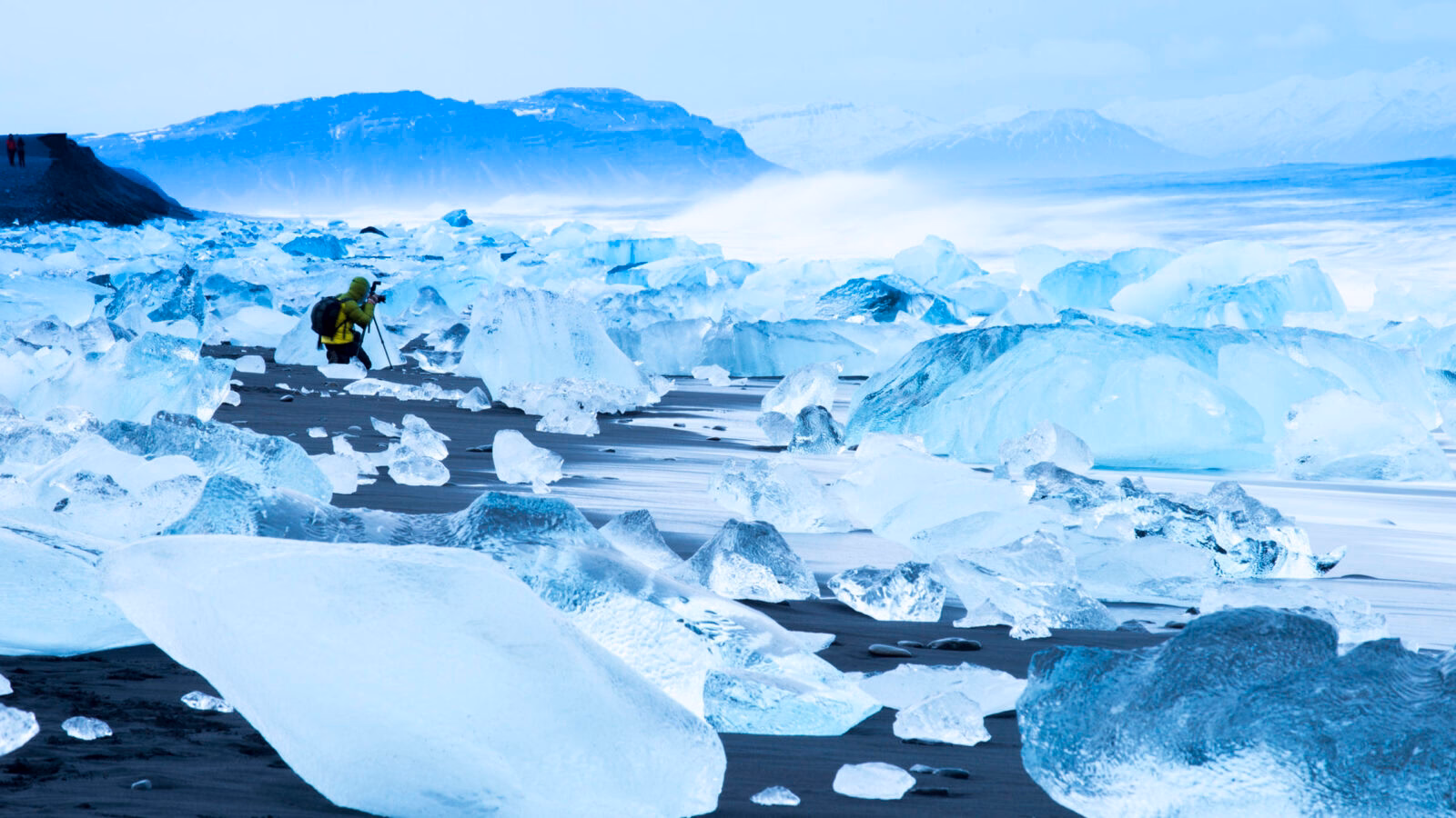 Traveller photographing broken ice which has washed up on the shore of Jokulsarlon Ice Beach, Iceland