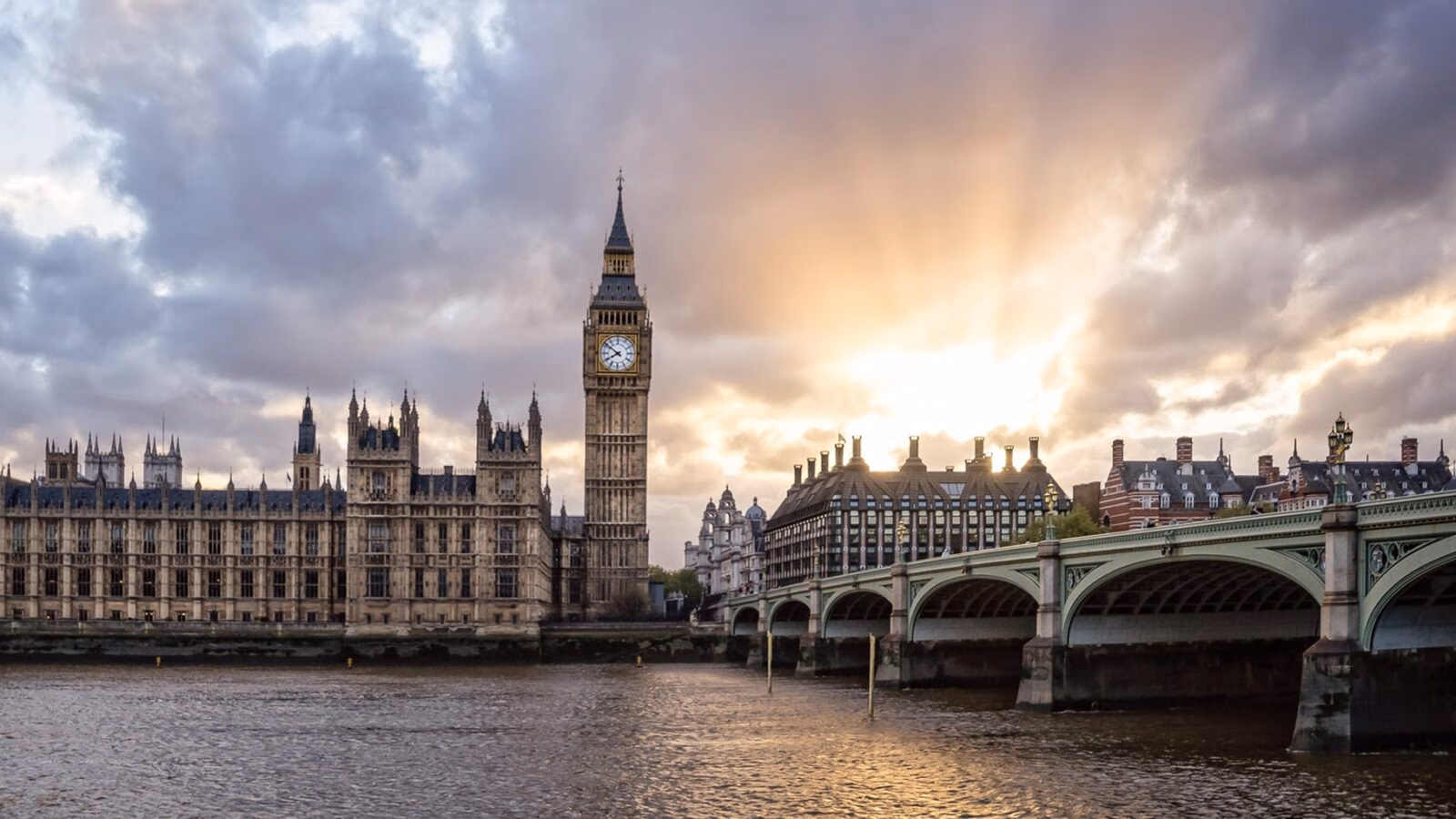 The Big Ben clock tower and Westminster Bridge over the River Thames in London under a dramatic sunset sky.