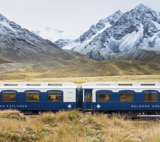 Exterior view of the blue Belmond Andean Explorer train carriages in a mountainous landscape.