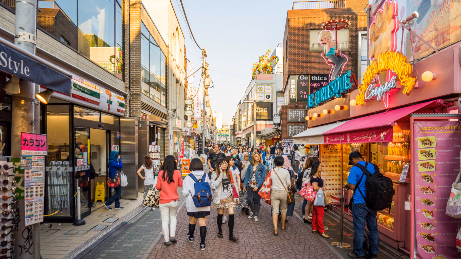 People walking down a busy city street with tall buildings and various retail storefronts and signage.