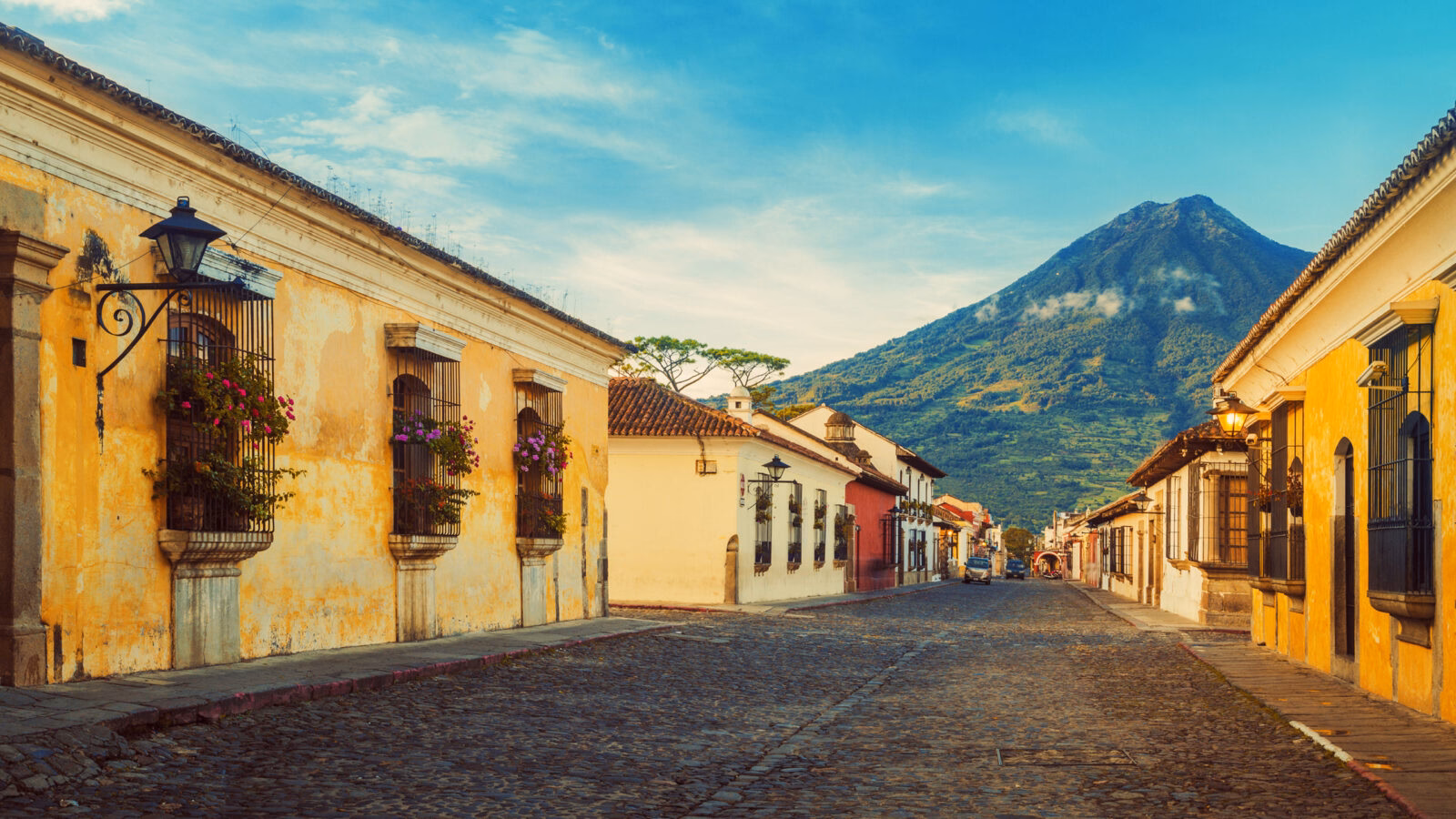 Cobblestone street of Antigua in Guatemala, lined by yellow houses with Acatenango volcano in the back