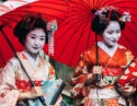 Private Japan Luxury Tours - Two maiko geisha walking on a street in Kyoto with red umbrellas