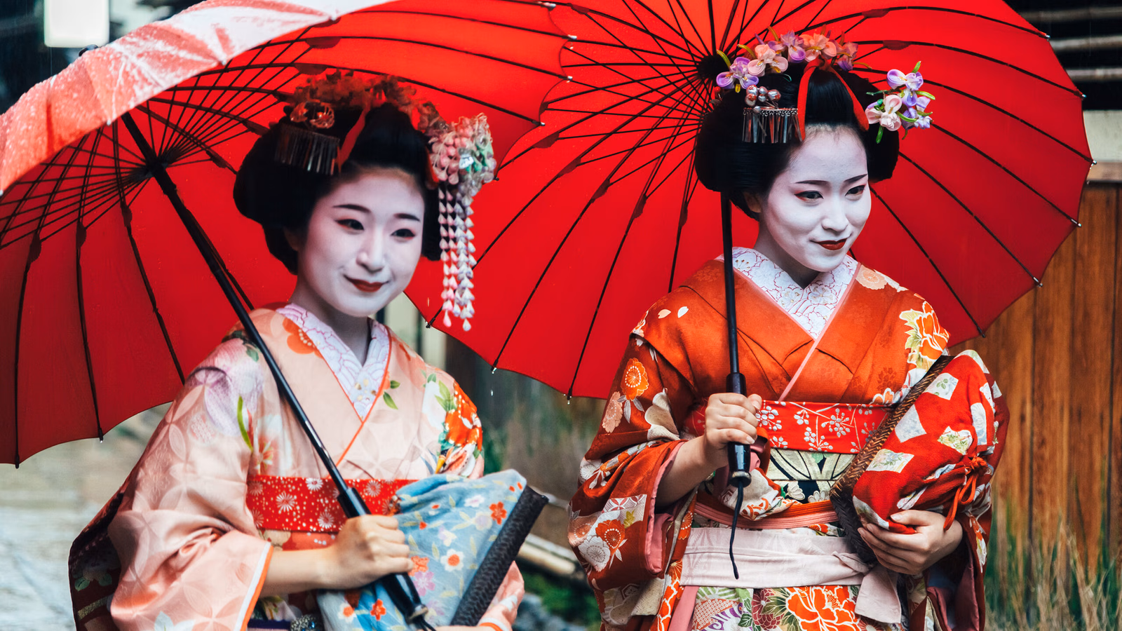 Private Japan Luxury Tours - Two maiko geisha walking on a street in Kyoto with red umbrellas