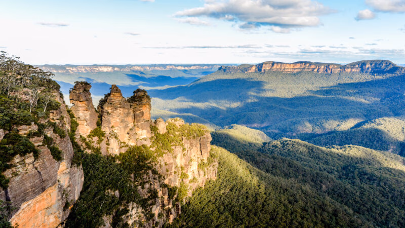 A scenic view of three large sandstone rock formations on a mountain ridge overlooking a deep, green valley.