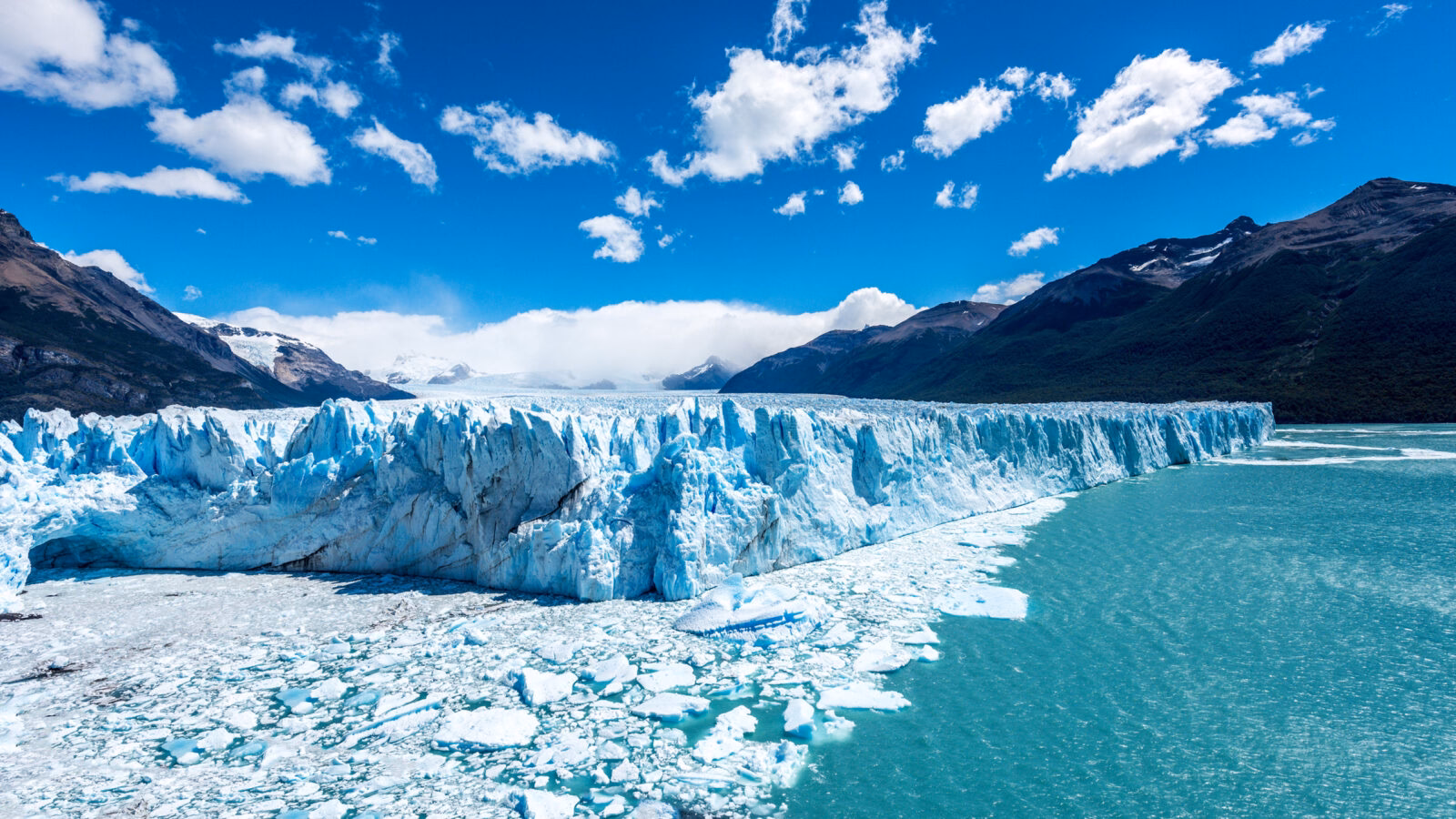 The massive, towering ice wall of the Perito Moreno Glacier meets a bright turquoise blue lake. Luxury Argentina holidays.