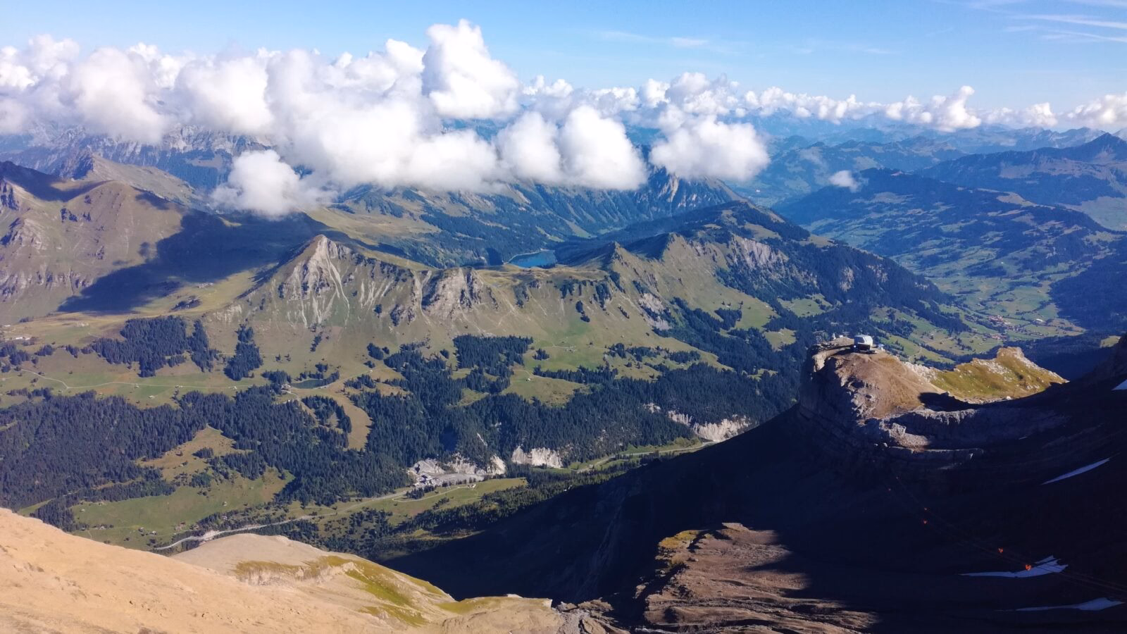 Aerial view of small grass-covered mountains and valleys in Switzerland with alpine lakes, and white fluffy clouds