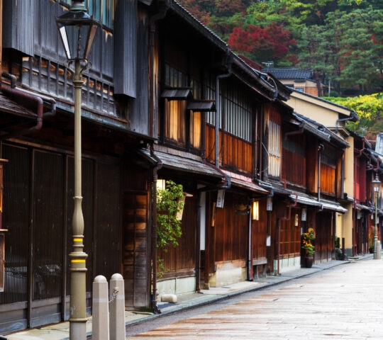 A narrow street in Japan lined with traditional dark wood buildings and a lamppost during the day.