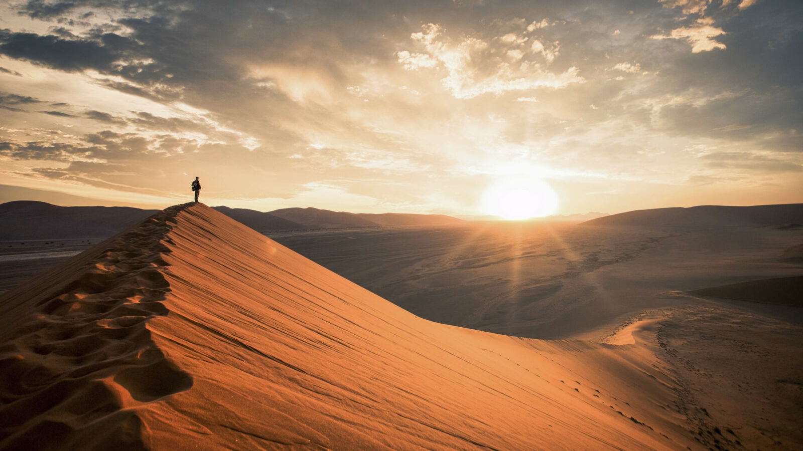 Dramatic sunrise in the Namibian desert with person standing and overlooking the great plains