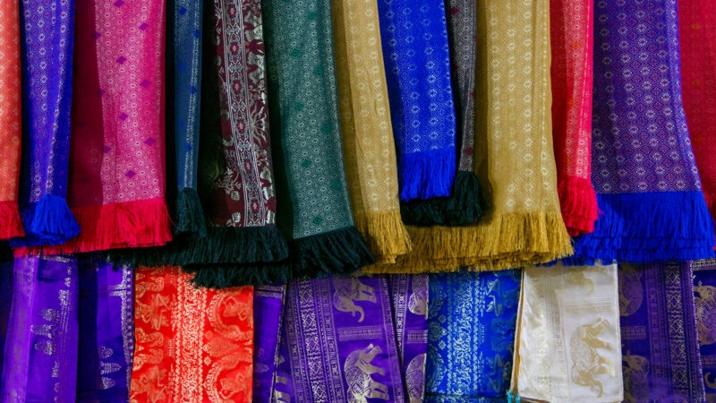 Close-up of various colorful silk scarves and textiles with traditional patterns hanging in a row.
