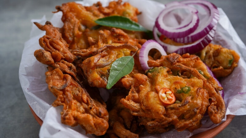 Golden fried onion and potato street food snack served with raw red onion and fresh herbs