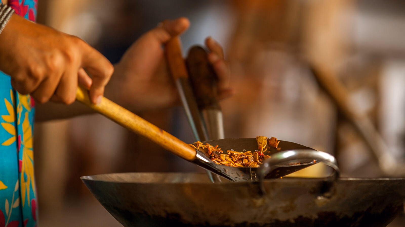 Close-up of hands cooking over a wok, a culinary experience included in luxury Indonesia holidays.