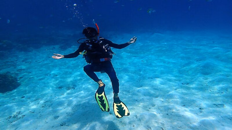 Scuba diver with yellow fins swimming over a sandy ocean floor during luxury Borneo tours.