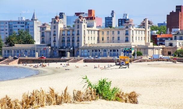Historic grand hotel building facing a sandy beach with a yellow lifeguard stand and people in the distance.