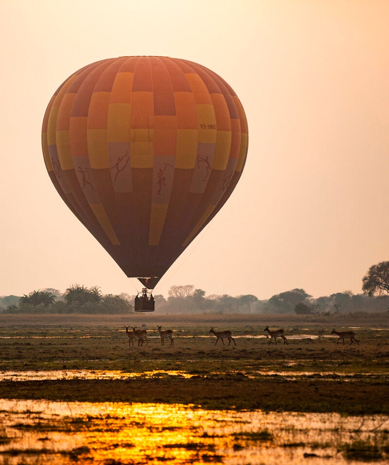 Hot air balloon flying over a landscape with wildlife during luxury Zambia trips.