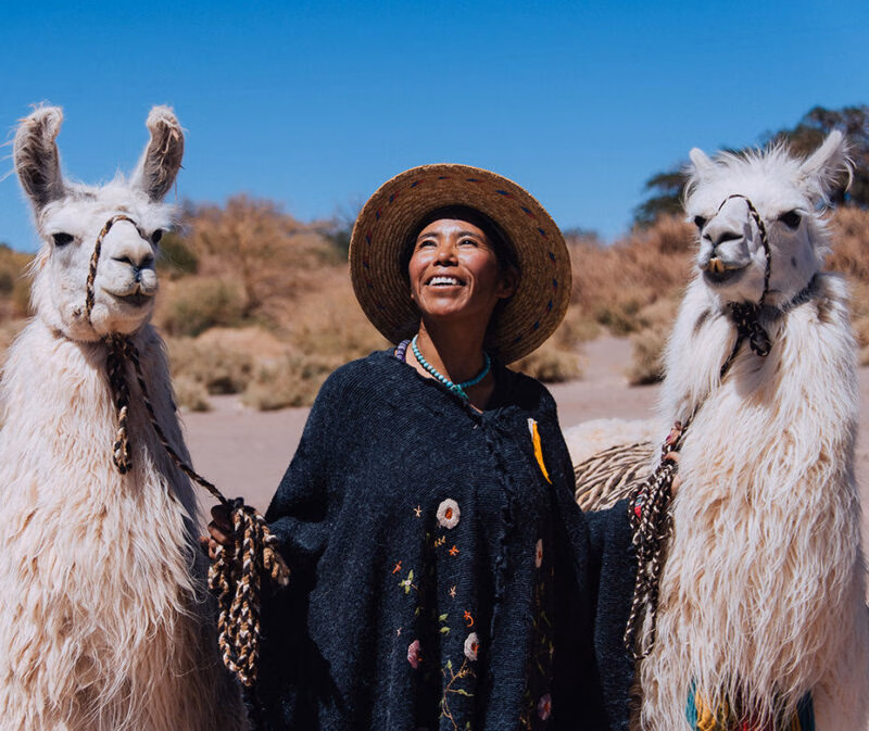 A woman smiling between two llamas under a clear blue sky on luxury Chile tours.