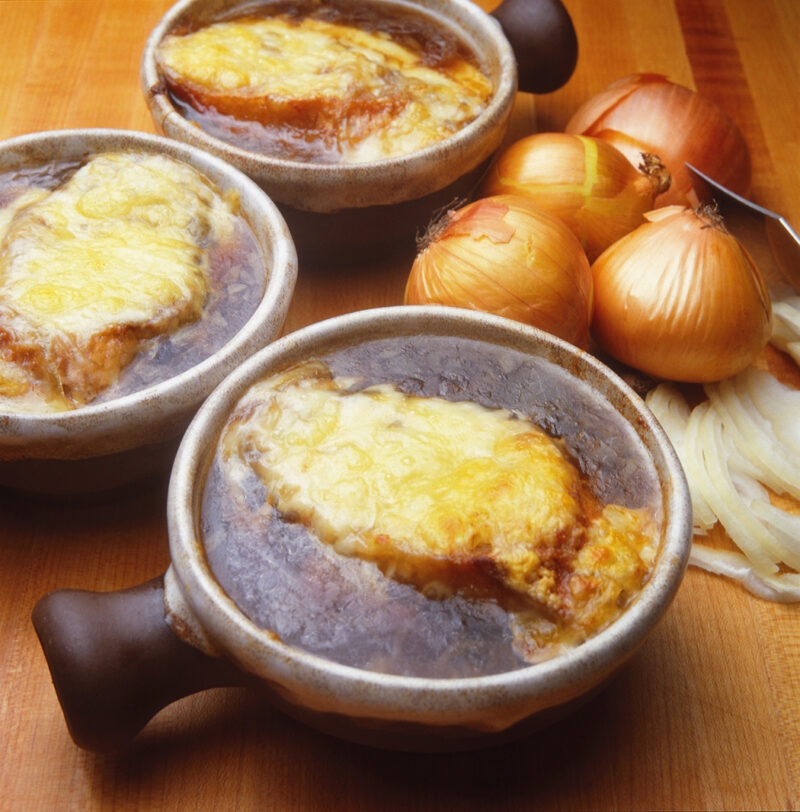 Ceramic bowls of hot French onion soup with melted cheese for luxury France holidays.