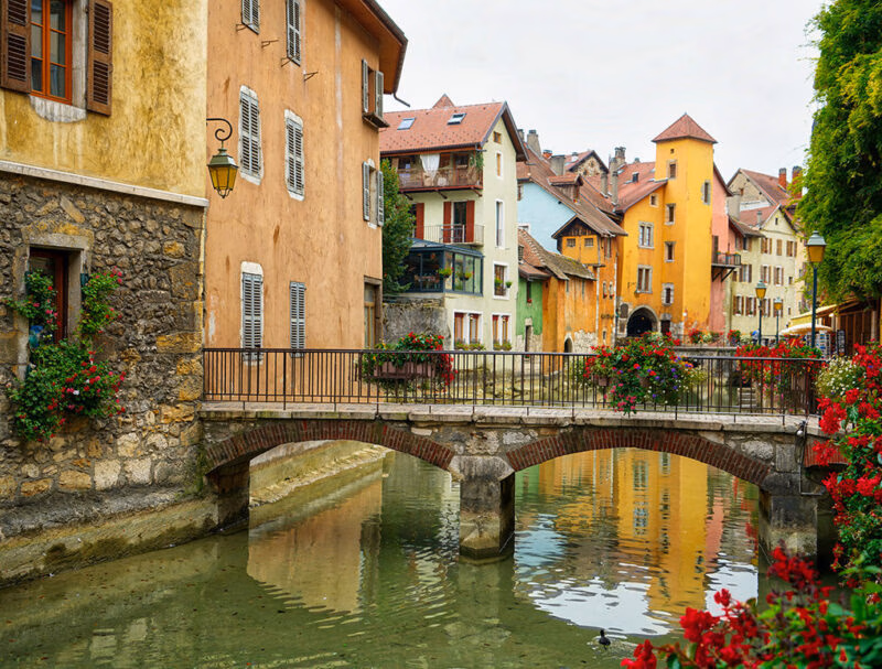 Colorful buildings reflected in a canal with flower-lined bridges on luxury France trips.