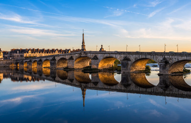 A historic arched stone bridge reflecting in a river at sunset during luxury France trips.