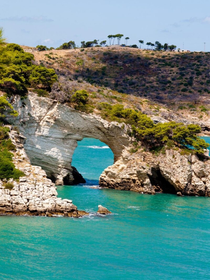 Luxury Italy Tours - Gargano national park in Puglia, Italy, with a dramatic rock archway eroded out of the coastline through which bright blue sea is visible