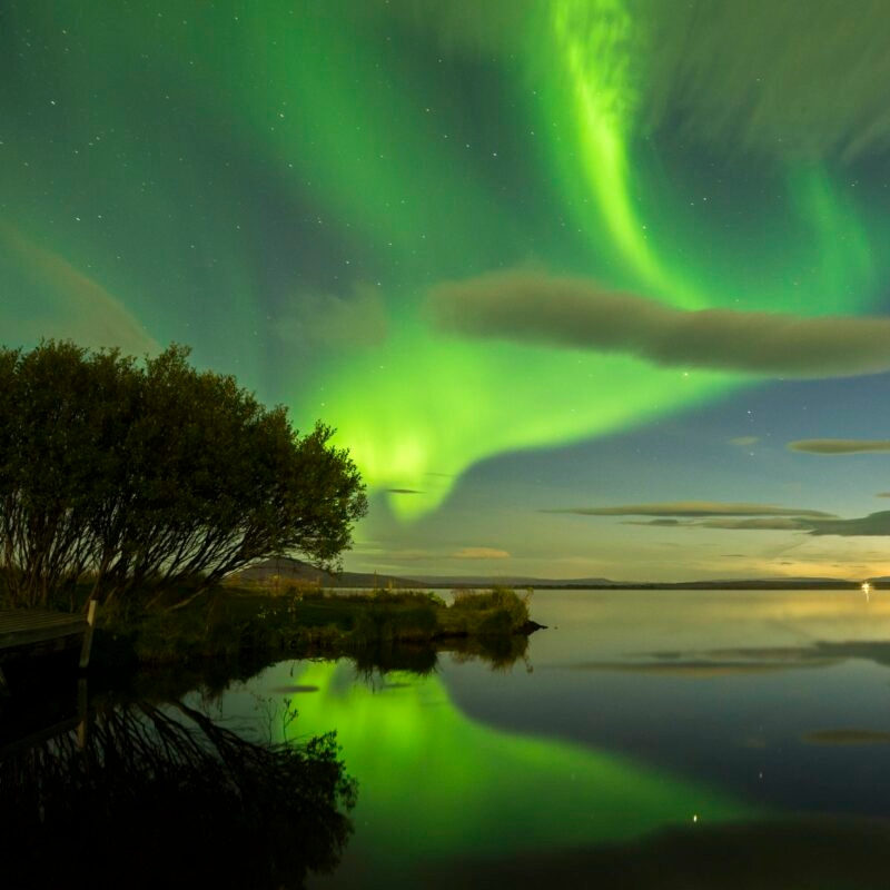Jacada Iceland - Green arcs of Northern Lights over a still body of water