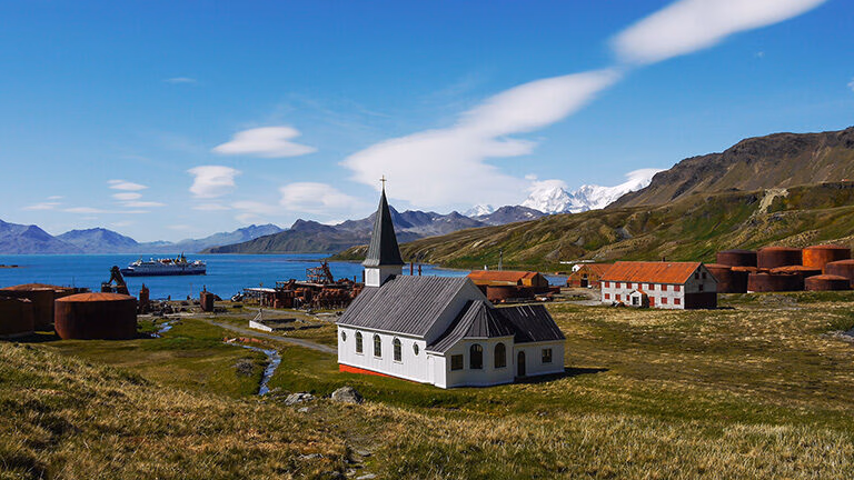 Wide view of the historic white church and rusty oil tanks at the Grytviken whaling station in South Georgia.