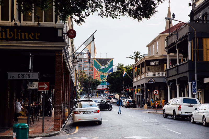 Luxury South African Tours - View of a city street with cars, pedestrians, and various shopfronts under a clear sky.