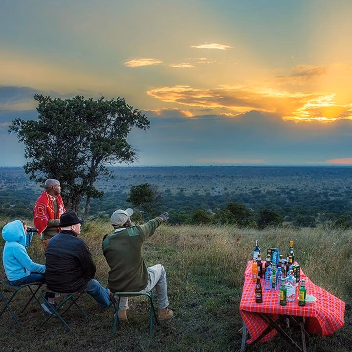 People sitting on a hillside with drinks on a red checkered table during a luxury Kenya family safari sunset.